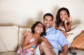 A father watches TV with his two daughters.