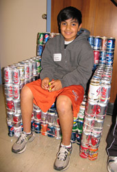 Boy sits in chair made of used soda cans.